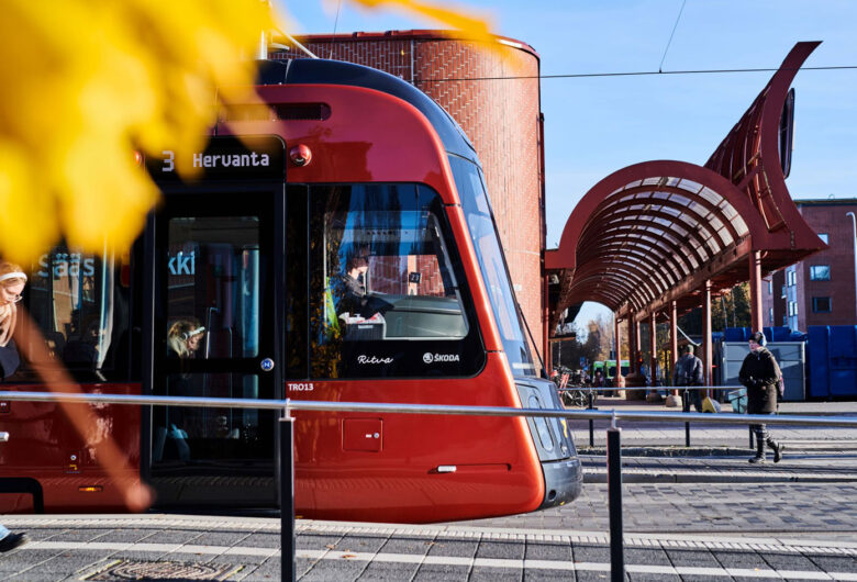 Näkymä Tampereen keskustasta, jossa punainen raitiovaunu ylittää siltaa Näsijärven rannalla.