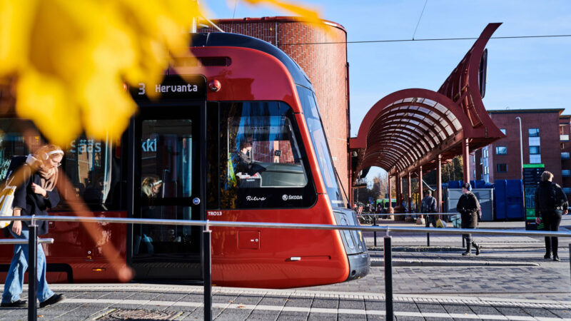 Näkymä Tampereen keskustasta, jossa punainen raitiovaunu ylittää siltaa Näsijärven rannalla.