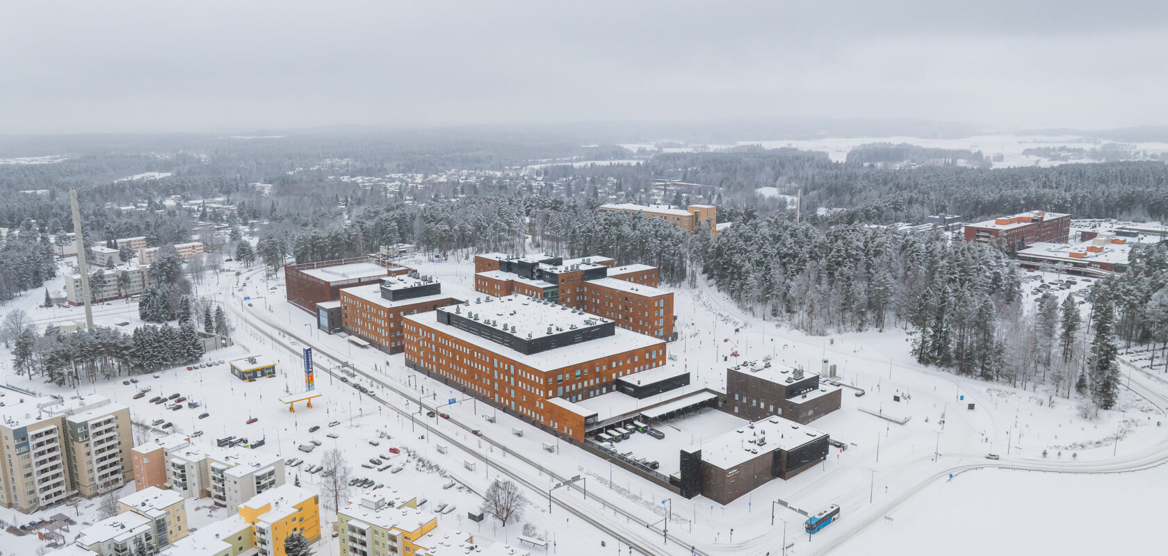 Aerial view of Ahvenisto Hospital, surrounded by forest and residential areas, in daylight during winter.