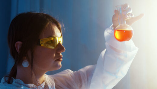 Laboratorioasuinen henkilö pitelee punaista nestettä sisältävää pyöreää labkapulloa.