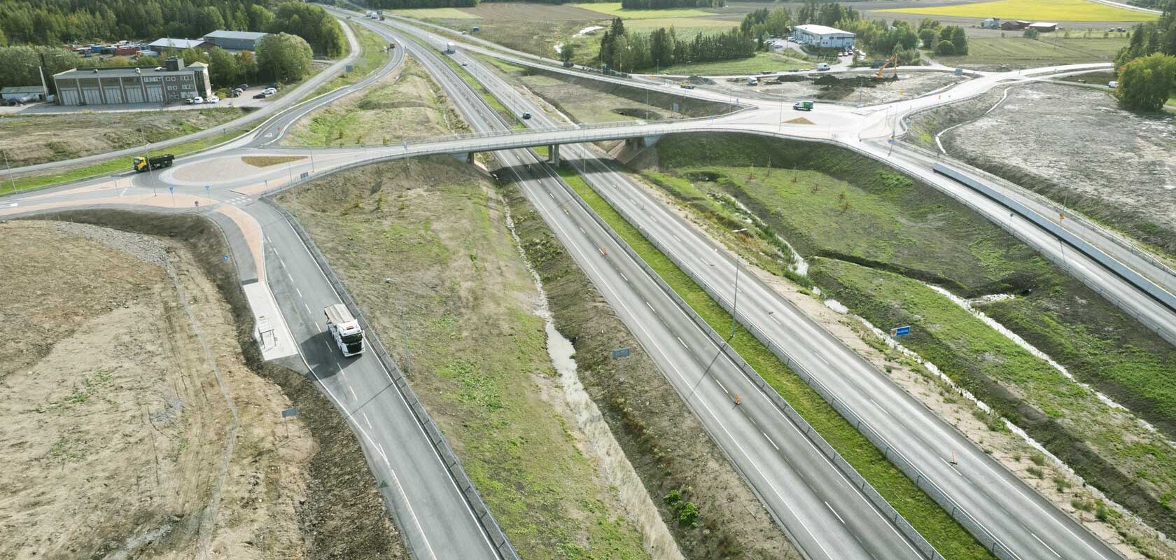 Ilmakuva moottoritie ja risteys lähellä metsää ja peltoja maalaismaisemassa.