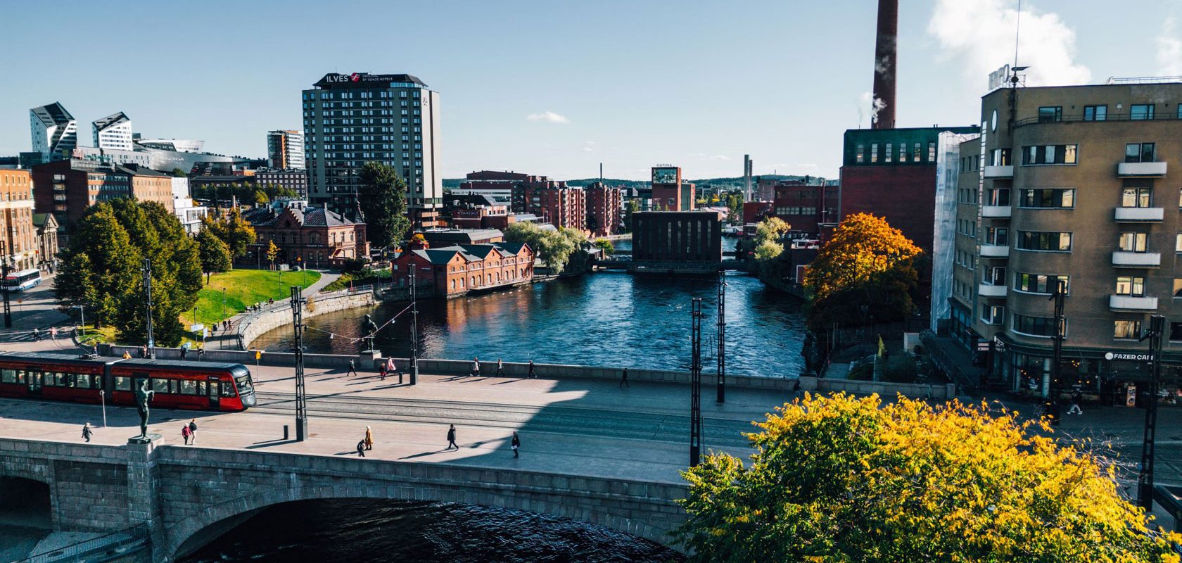 Näkymä Tampereen keskustasta, jossa punainen raitiovaunu ylittää siltaa Näsijärven rannalla.