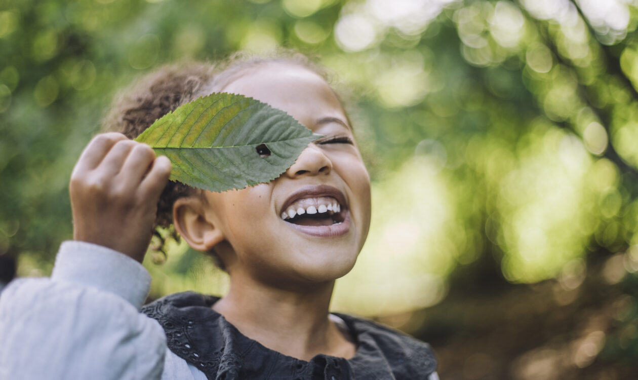 Tyttö katsoo suuren puunlehden läpi olevasta reiästä