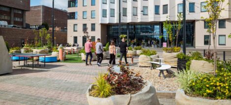 Ihmisiä kävelemässä Ilmalantori-aukiolla Helsingissä, moderni rakennus taustalla.