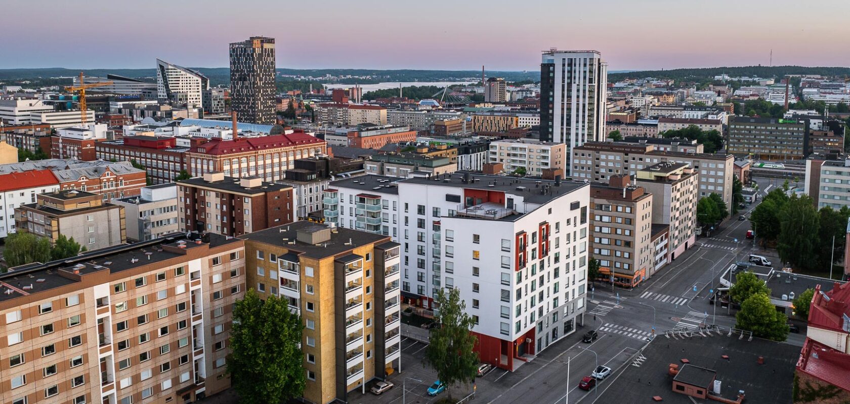 Ilmakuva kaupunkimaisemasta, jossa on erilaisia rakennuksia, mukaan lukien asuin- ja liikekiinteistöjä. Näkyvissä on useita korkeita rakennuksia, katuja ja risteyksiä.