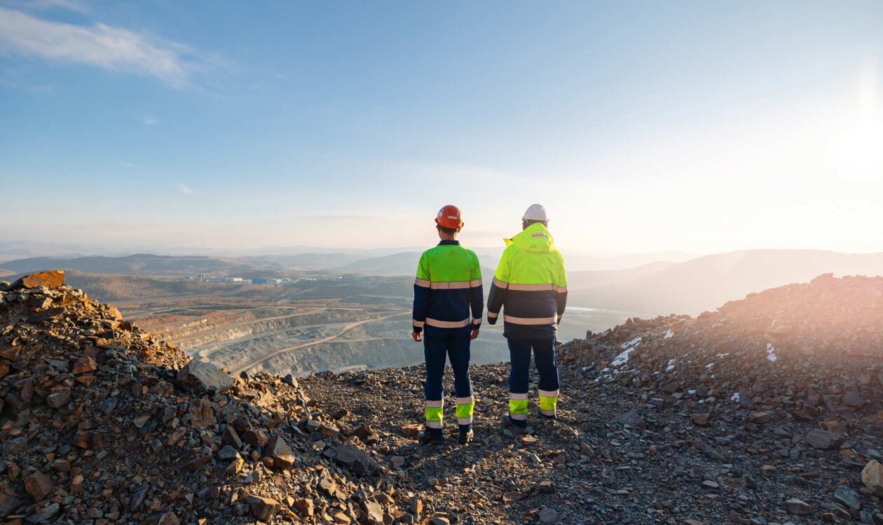 Kaksi rakennustyöntekijää seisoo louhoksella katsellen maisemaa auringonnousun aikaan.