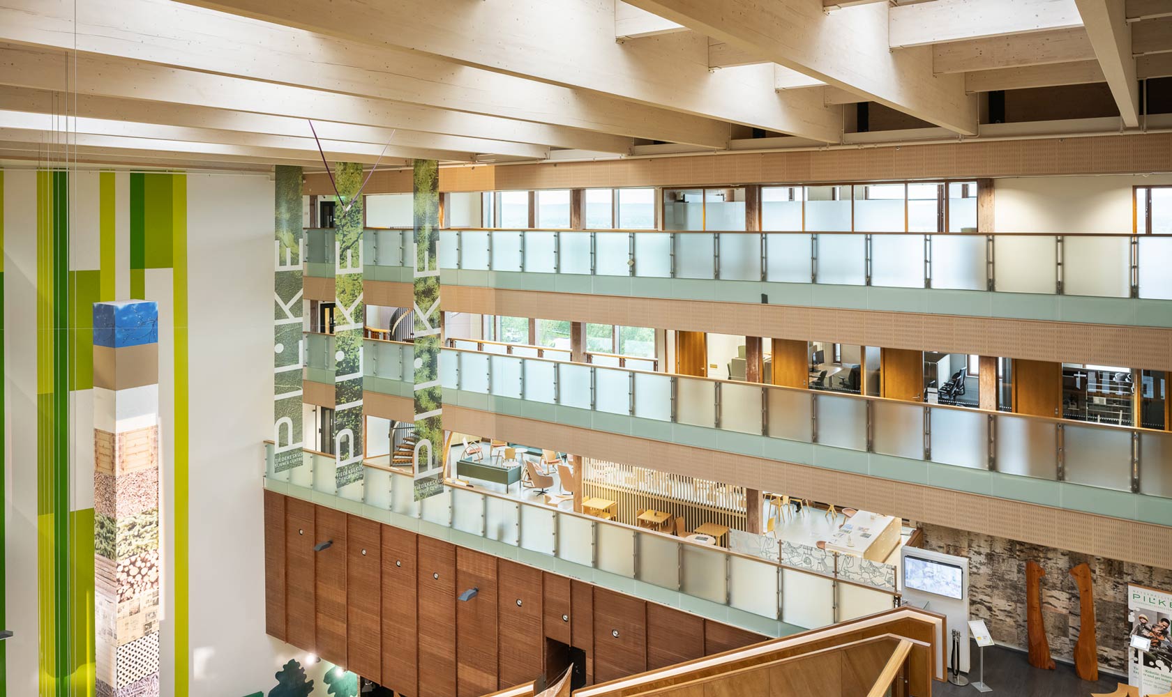 Modernin monikerroksisen rakennuksen sisätila, jossa on avoin atrium. Rakennuksessa on useita kerroksia lasikaiteilla ja puukoristeilla.