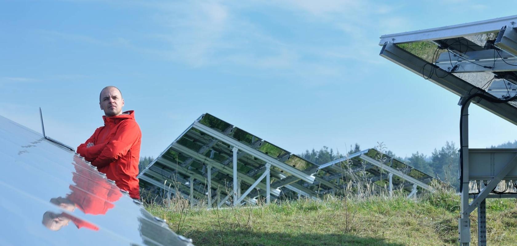 Punatakkinen mies kannettavan tietokoneen kanssa aurinkopaneelikentällä.