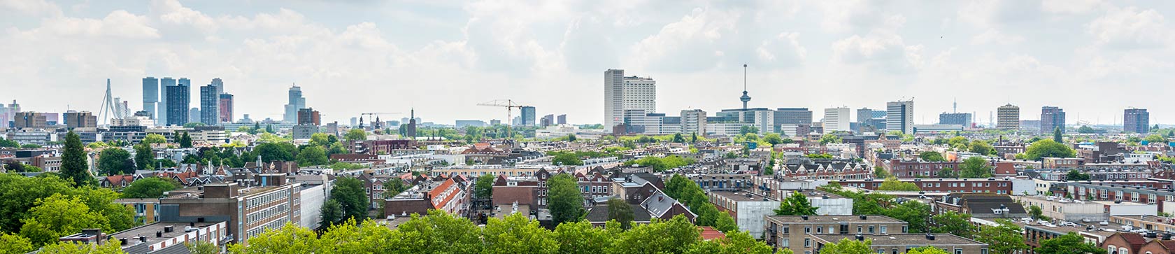 Kaupungin horisontti, jossa taustalla näkyy korkeita rakennuksia ja pilvenpiirtäjiä, etualalla matalampia asuinrakennuksia. Taivas on osittain pilvinen.