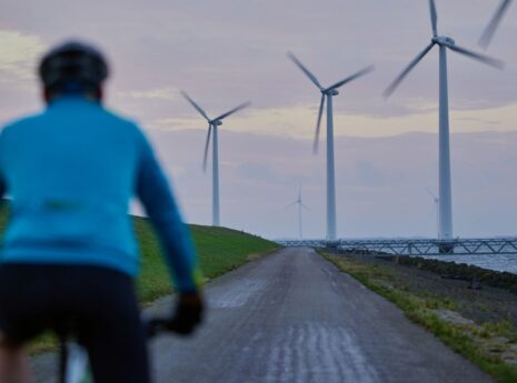 Man cycling on a coastal embankment, wind turbines in the background