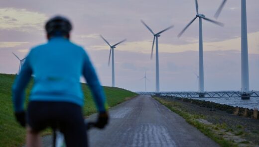 Man cycling on a coastal embankment, wind turbines in the background
