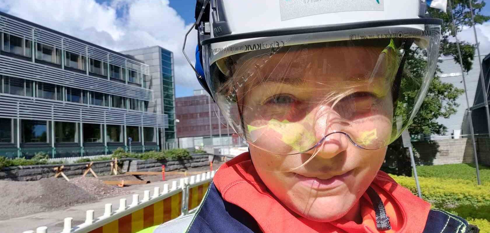 Suunnittelupäällikkö Outi Toivonen työmaakypärä päässä ja suojalasit silmillä, raitiovaunutyömaa taustalla