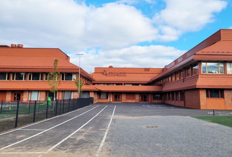 Moderni tiilirakennus kirkkaan sinisen taivaan alla, koulun piha-alueella juoksurata.