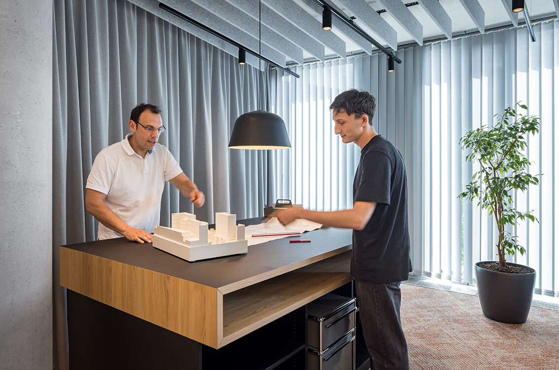 Kaksi henkilöä pienoismallin äärellä toimistosta