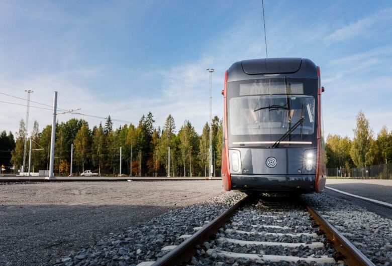 Tampereen Ratikka kuvattu edestäpäin hiekkakentällä, taustalla puita