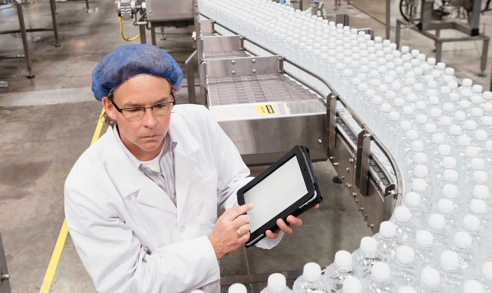 Työntekijä vesipullotehtaassa tarkastaa tuotantolinjaa tabletilla.