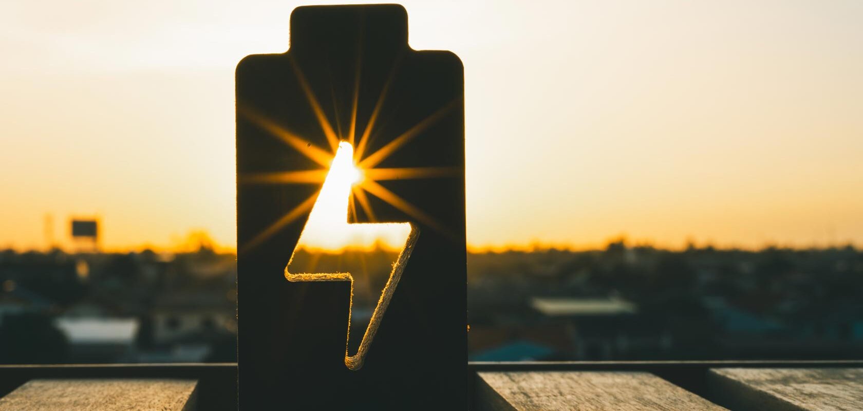 Sunset silhouette of battery cutout with lightning bolt shape, symbolizing solar power energy.