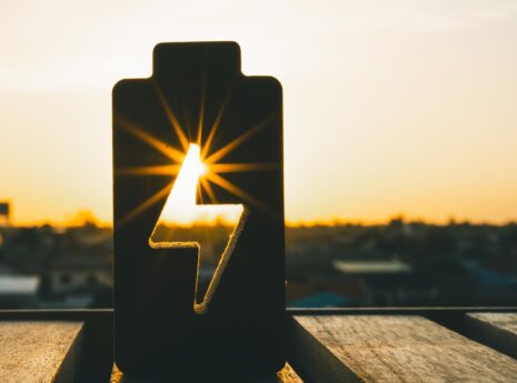Sunset silhouette of battery cutout with lightning bolt shape, symbolizing solar power energy.