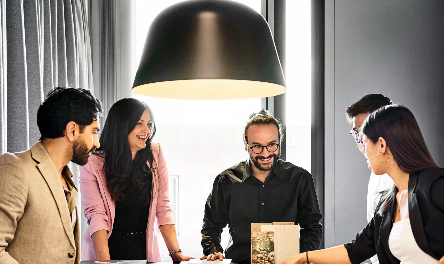 Ryhmä ihmisiä kokouksessa modernissa toimistossa, suuri musta valaisin pöydän yläpuolella.