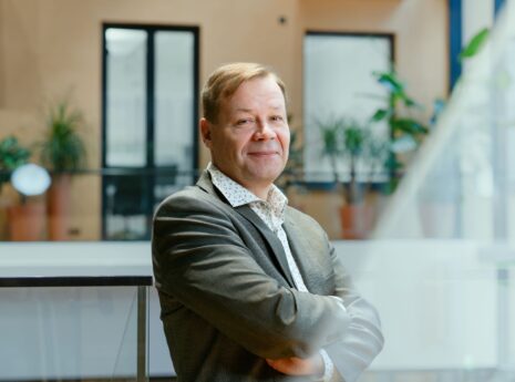 Hymyilevä keski-ikäinen mies puvun takissa kädet puuskassa rinnan päällä