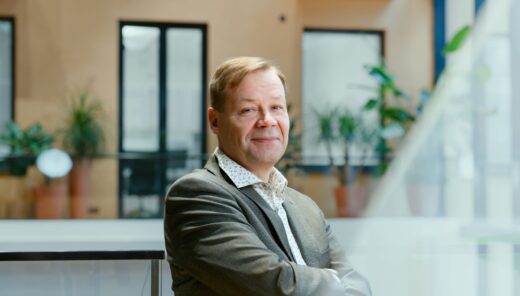 Hymyilevä keski-ikäinen mies puvun takissa kädet puuskassa rinnan päällä