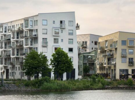 Valkoinen, vaalenakeltainen sekä punatiilinen kerrostalo veden äärellä, matalat, maksimissaan viisikerroksiset talot ja lasitetut, 2020-luvun tyyliset parvekkeet.