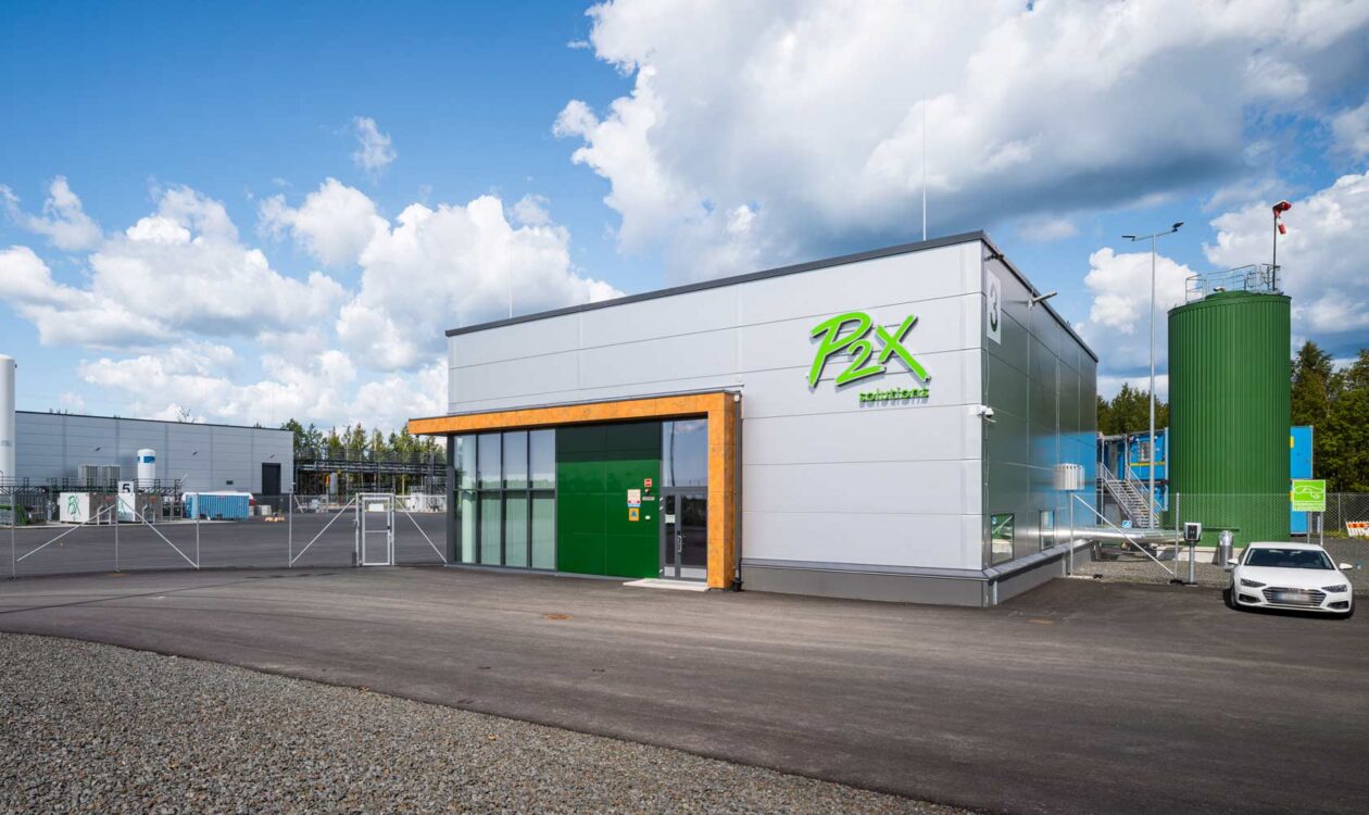 P2X Solutions-toimipiste, moderni teollisuusrakennus ja säiliö ulkona aurinkoisella säällä.