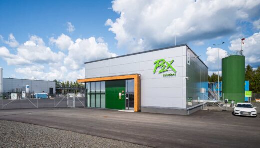 P2X Solutions-toimipiste, moderni teollisuusrakennus ja säiliö ulkona aurinkoisella säällä.