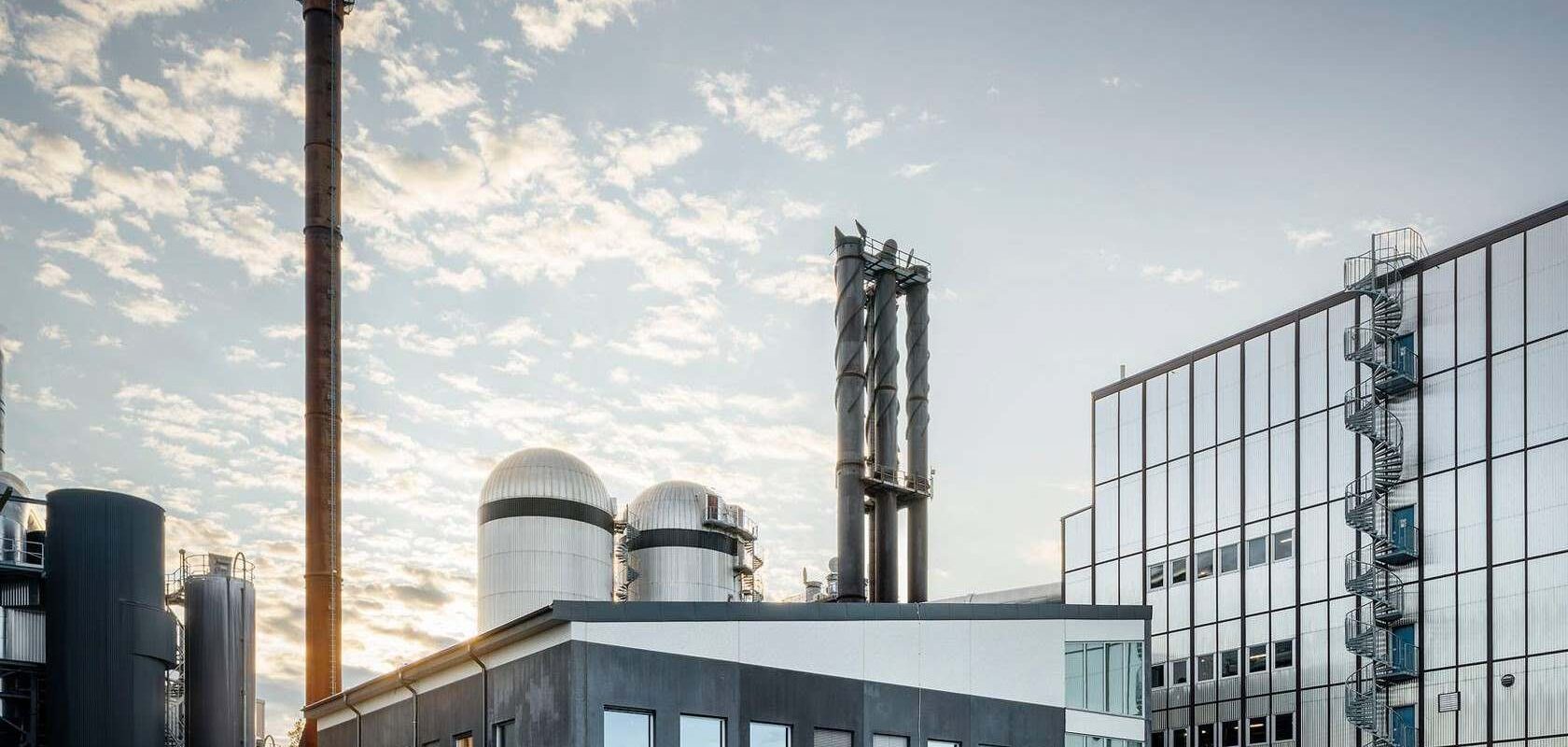 Taka-alalla bioenergialaitoksen kattiloita ja savupiippu, edessä energiayhtiön toimistotiloja, ilta-aurinko paistaa