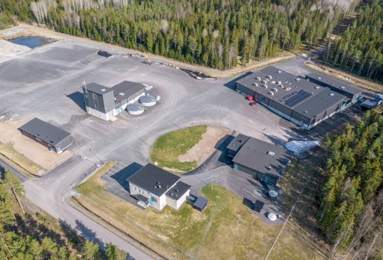 Aerial view of industrial facility surrounded by forest with multiple buildings and paved roads.