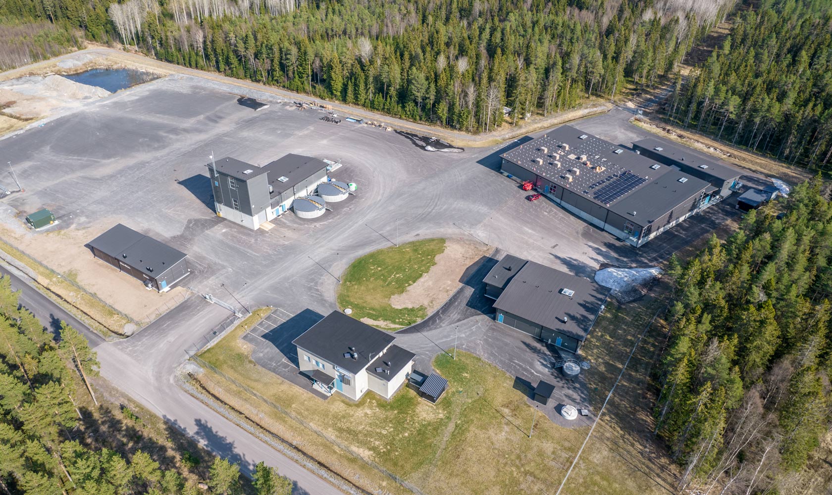 Aerial view of industrial facility surrounded by forest with multiple buildings and paved roads.