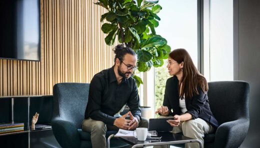 Kaksi ihmistä keskustelemassa modernissa toimistossa ison kasvin vieressä.