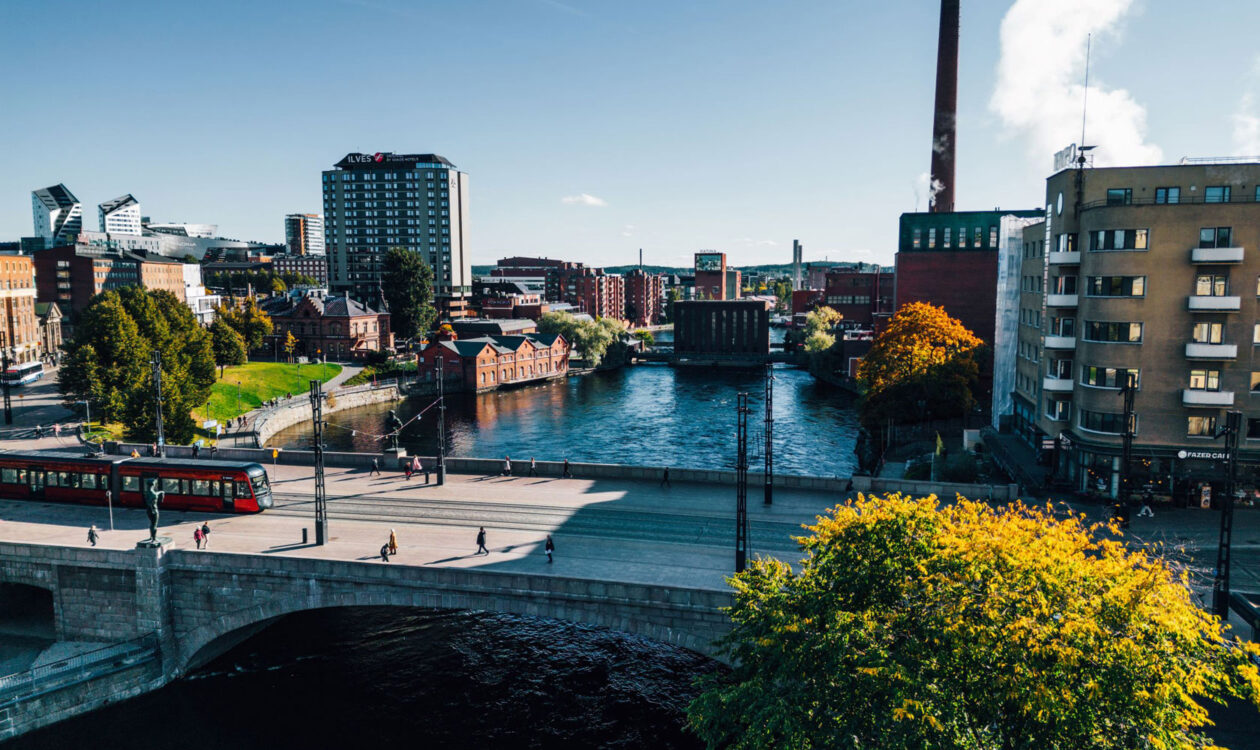 Näkymä Tampereen keskustasta, jossa punainen raitiovaunu ylittää siltaa Näsijärven rannalla.