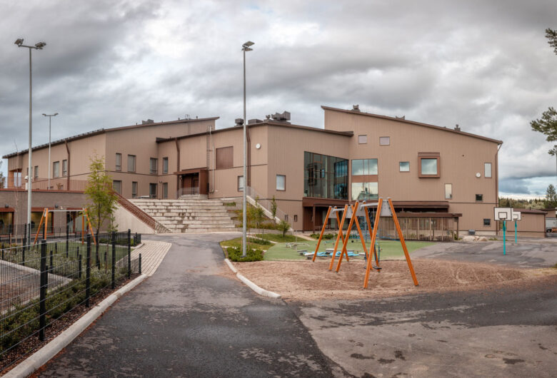 Uusi vaalea koulurakennus, etualalla leikkipaikka ja koripallokenttä.