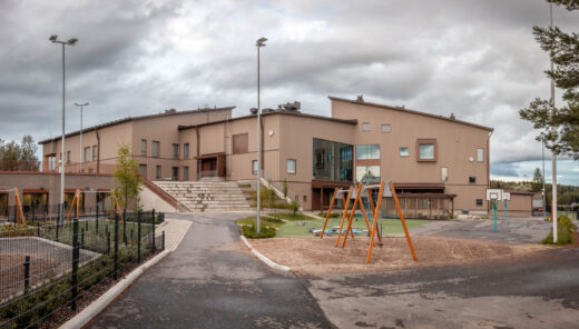Modern school building with playground swings, basketball court, and cloudy sky background.
