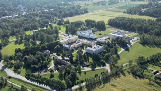 Aerial view of buildings and green landscape surrounded by trees in countryside.