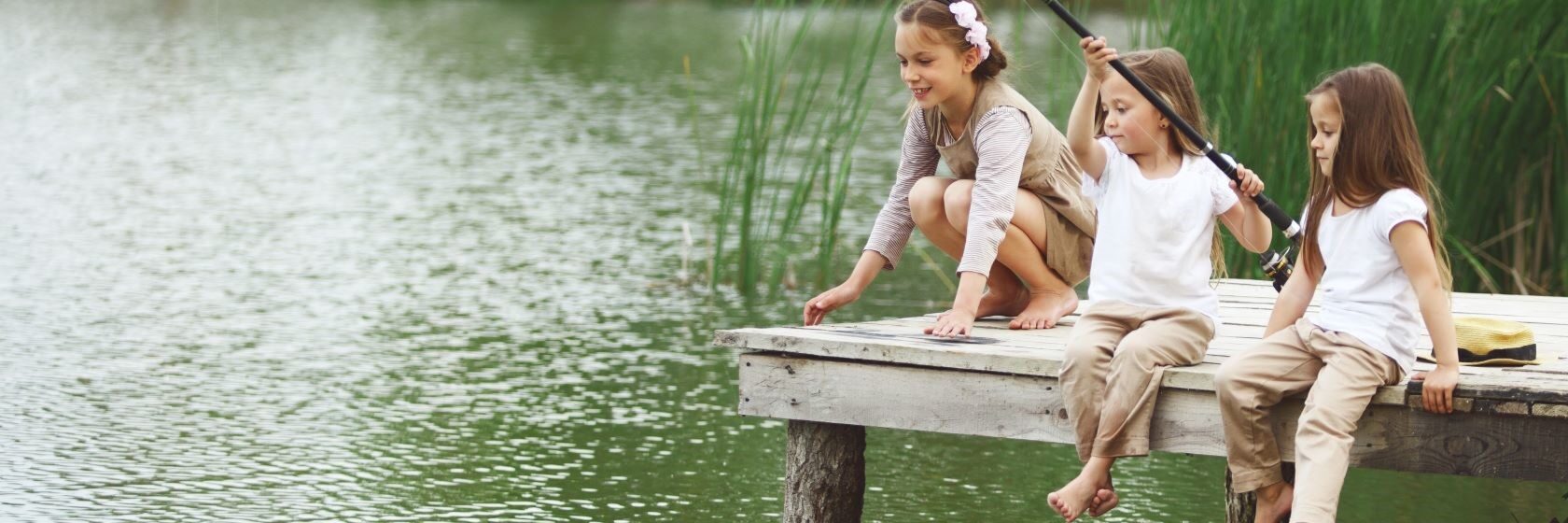 Three little girls by a pond fishing