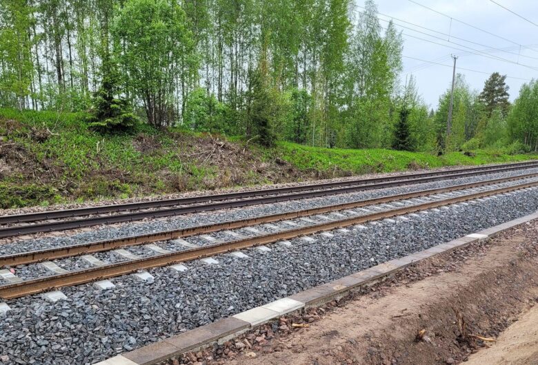 Railway tracks next to a lush green forest on a cloudy day.