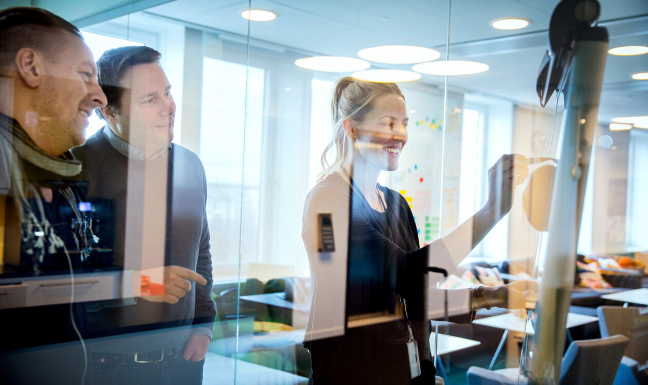 Business meeting: colleagues collaborating and writing ideas on a glass board in a modern office.