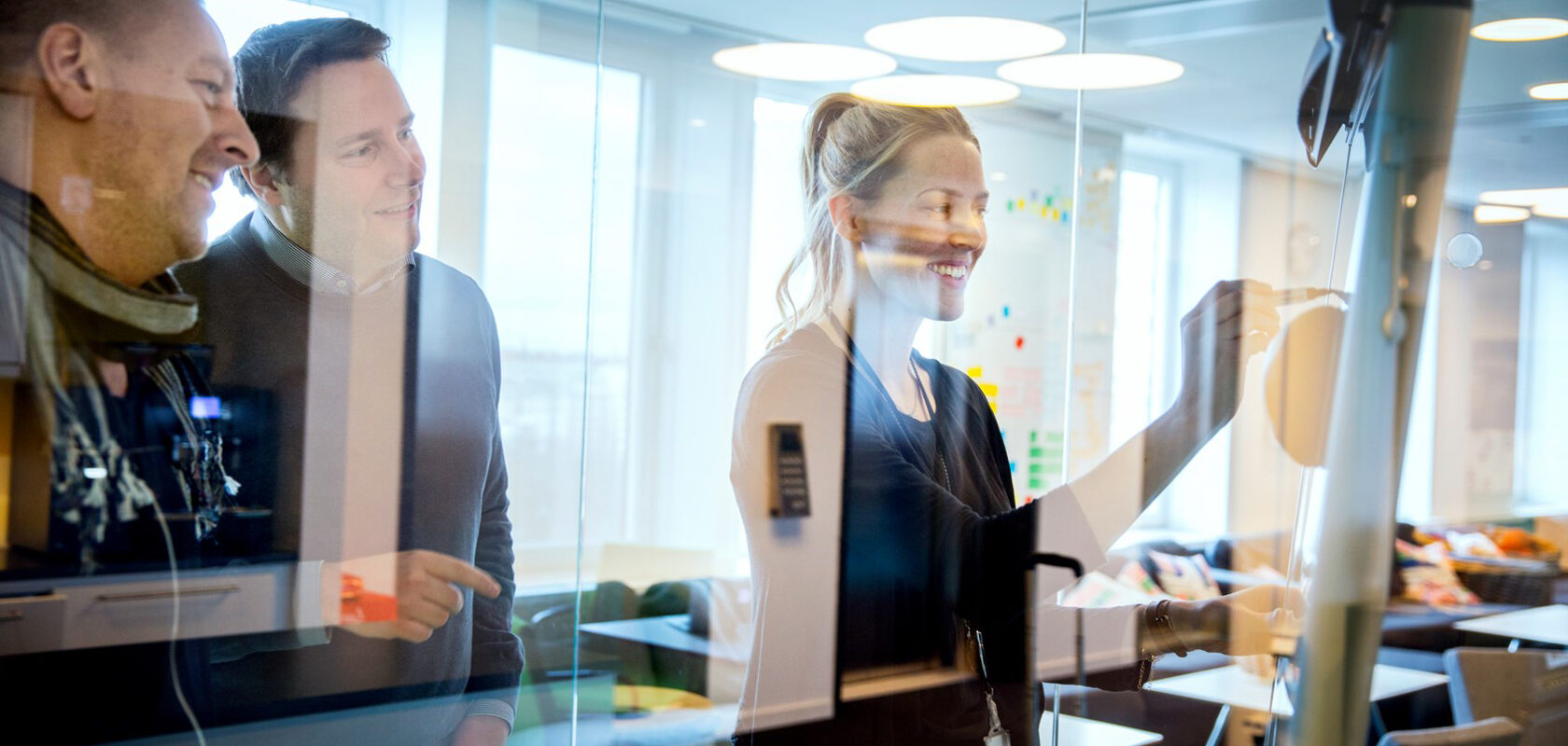Business meeting: colleagues collaborating and writing ideas on a glass board in a modern office.