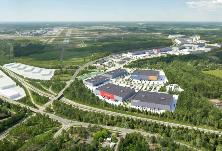Aerial view of industrial buildings and green forested area near an airport runway on a clear day.