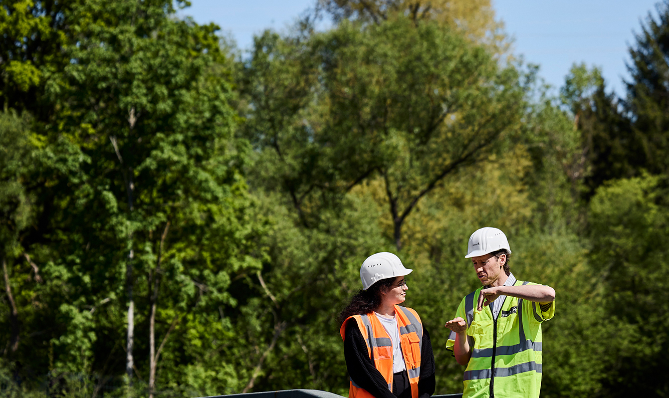 Kaksi arkeologia keskustelemassa metsän laidalla. Taustalla vihreää metsää.