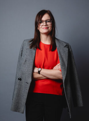 Henkilökuva, tummahiuksinen nainen seisoo kädet puuskassa jakku hartioillaan.