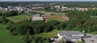 Aerial view of sports fields and running track near a small town surrounded by forest.