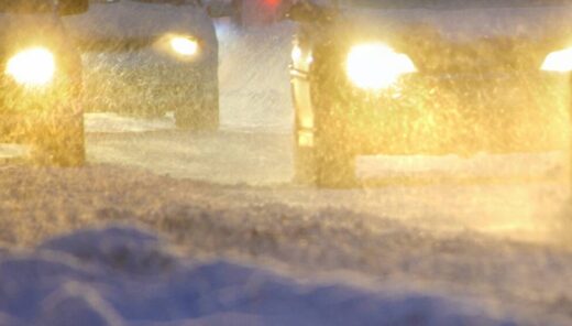 Autoja ajamassa lumisateessa pimeällä.