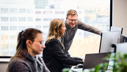 Toimistotyöntekijät tietokoneilla avokonttorissa keskustelemassa projektista.