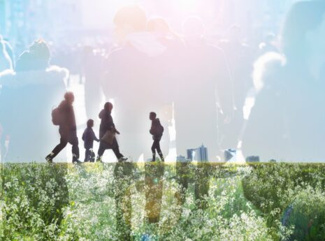 Valoisassa kollaasissa päällekkäin ihmishahmoja kävelemässä ja vihreä niitty sinistä taivasta vasten