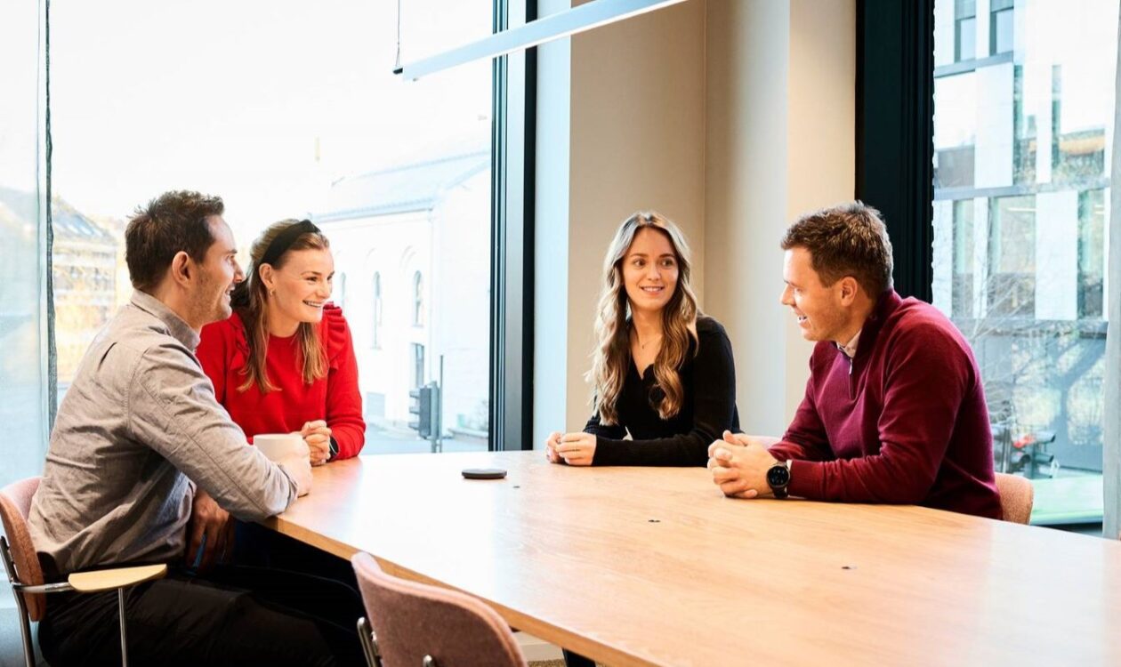 Four adults are seated together around a conference table in a meeting room.