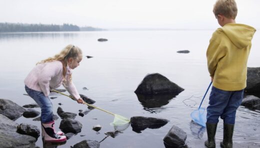 Kaksi lasta kumisaappaat jalassa leikkivät haaveilla merenrannassa.