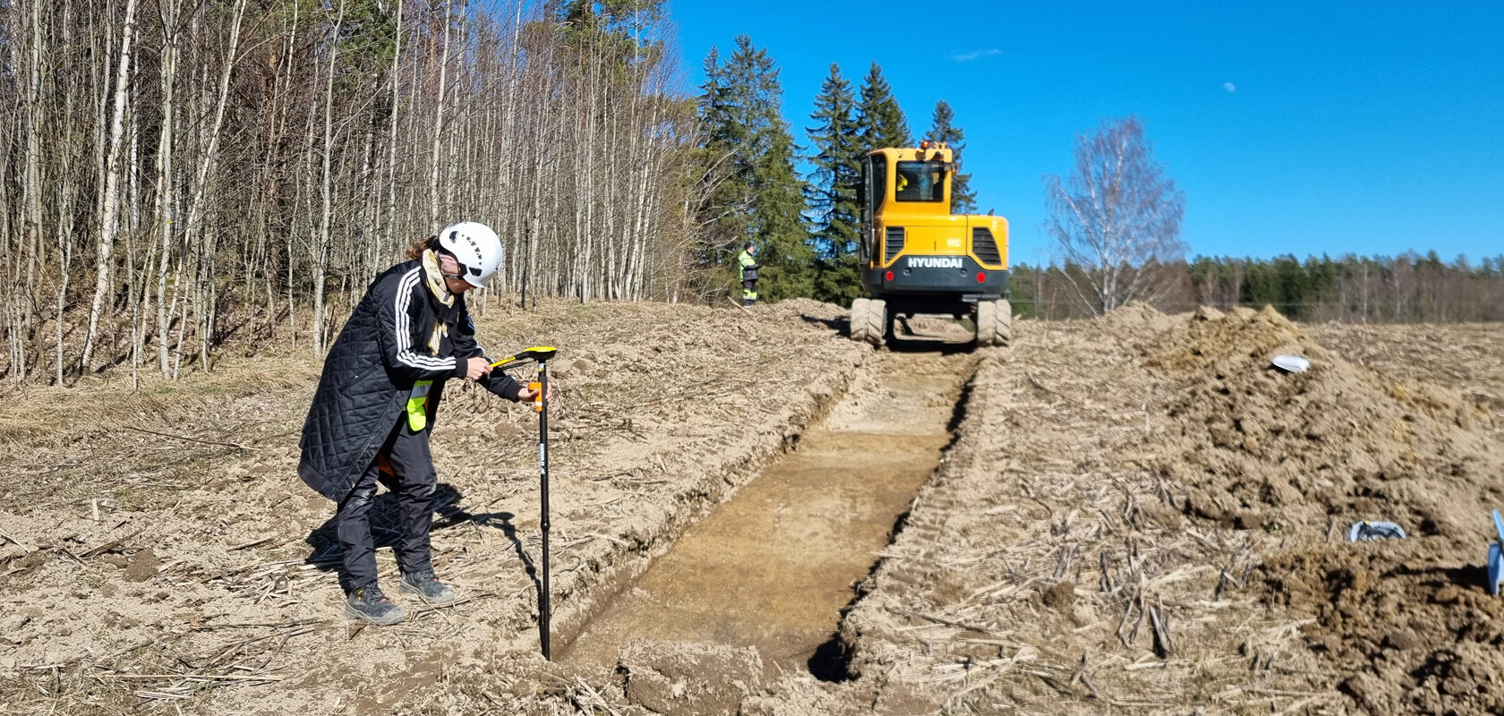 Archaeologist surveying trench with excavator on rural construction site
